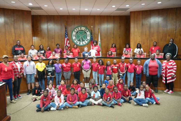 Many kids wearing red shirts and red ribbons smiling with the Mayor.